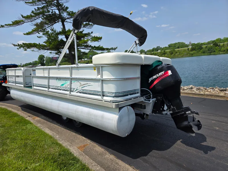 Slide: The Image of 2000 Odyssey Pontoons 2505 Millennium on trailer by a lake, featuring Mercury outboard motor. - 1