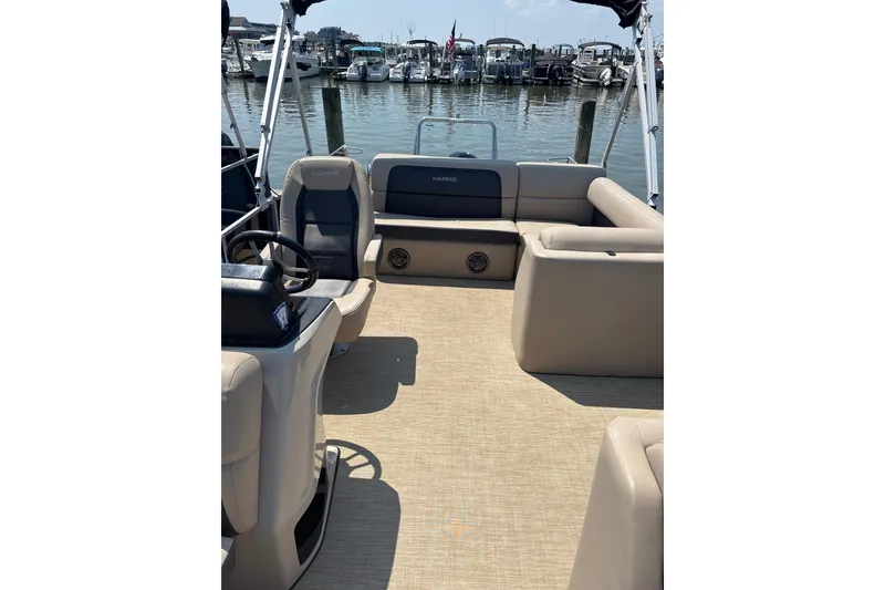 Slide: The Image of 2024 Harris HCX23 pontoon boat interior with beige seating and steering wheel, docked at marina. - 5