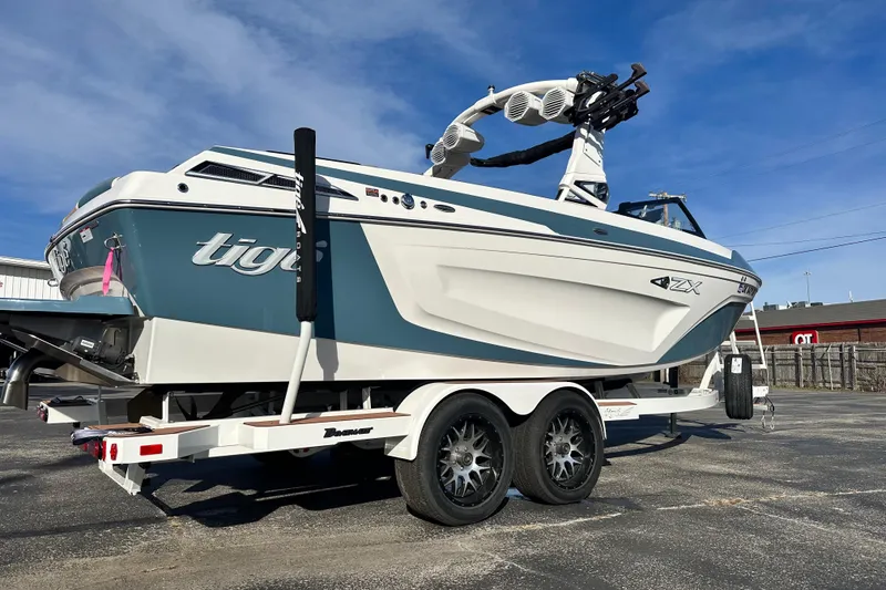 Slide: The Image of 2023 Tigé 23ZX boat on trailer, blue and white design, parked outdoors. - 2