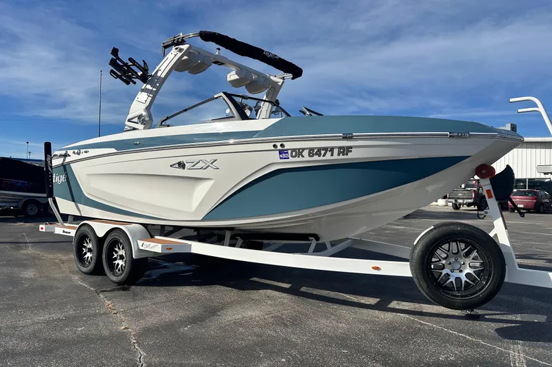 Slide: The Image of 2023 Tigé 23ZX boat on trailer, blue and white design, parked outdoors. - 3