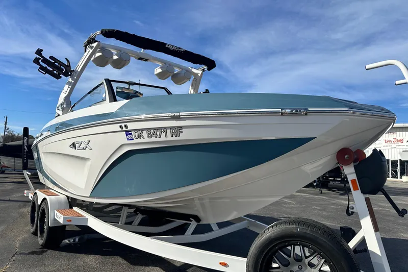 Slide: The Image of 2023 Tigé 23ZX boat on trailer, blue and white design, parked outdoors. - 4