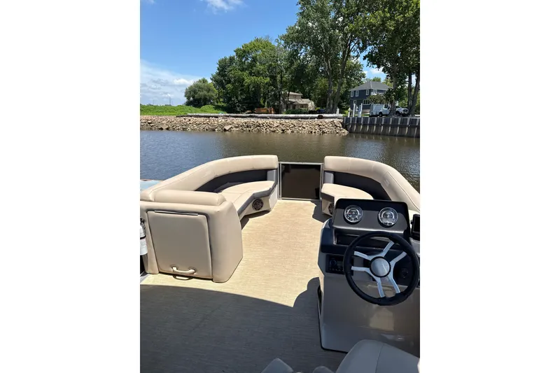 Slide: The Image of 2024 Harris HCX23 pontoon boat interior with steering wheel and seating, docked by a scenic river. - 6