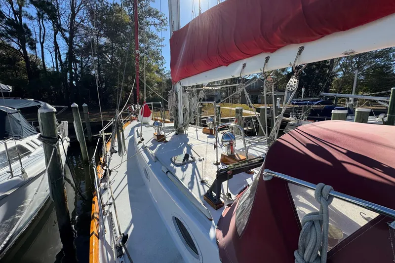 Slide: The Image of 1997 Creekmore Cutter sailboat docked, featuring red sail cover and wooded marina backdrop. - 34