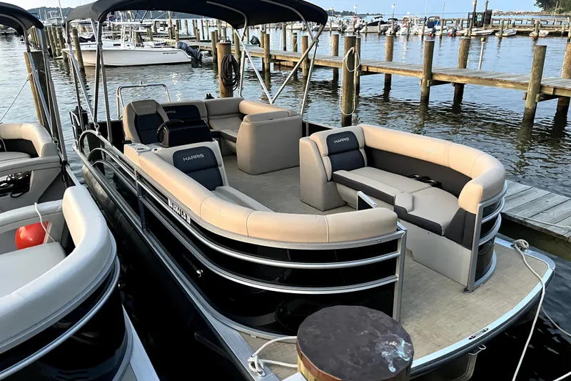 The Image of 2024 Harris HCX23 pontoon boat docked at a marina, featuring spacious seating. - 1