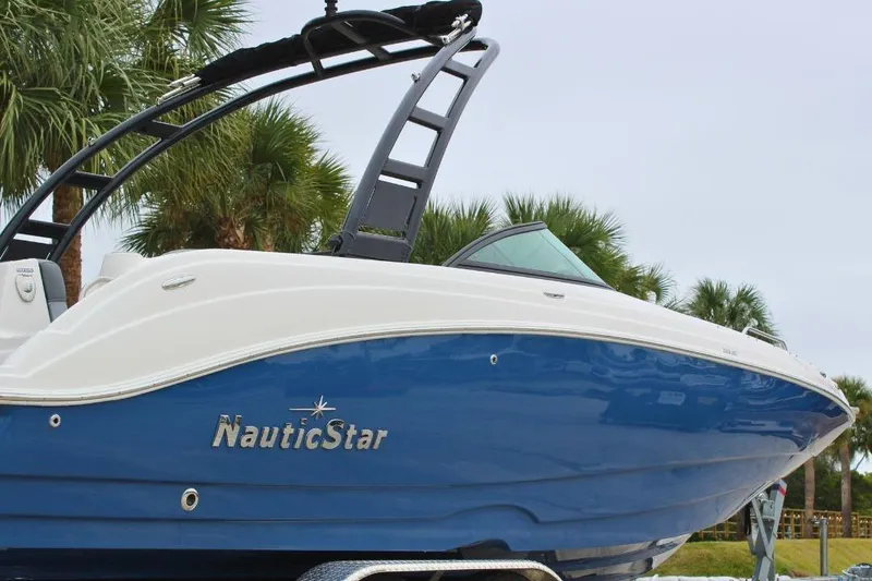 Slide: The Image of 2023 NauticStar 243 DC Deck boat with blue hull, parked near palm trees. - 6