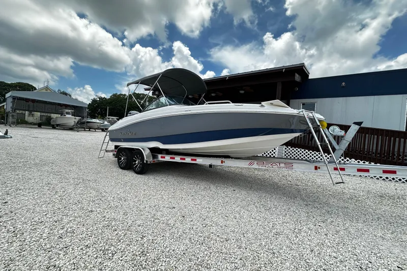 The Image of 2024 NauticStar 203 DC Deck boat on trailer, parked outdoors under cloudy sky. - 1