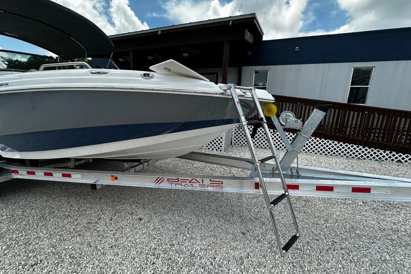 Slide: The Image of 2024 NauticStar 203 DC Deck boat on trailer with ladder, parked outdoors. - 17