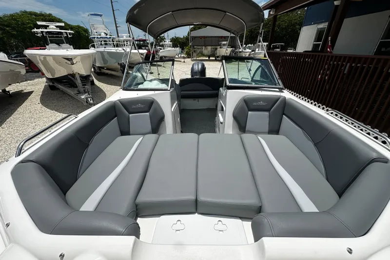 Slide: The Image of 2024 NauticStar 203 DC Deck boat with spacious seating and canopy in a marina. - 7