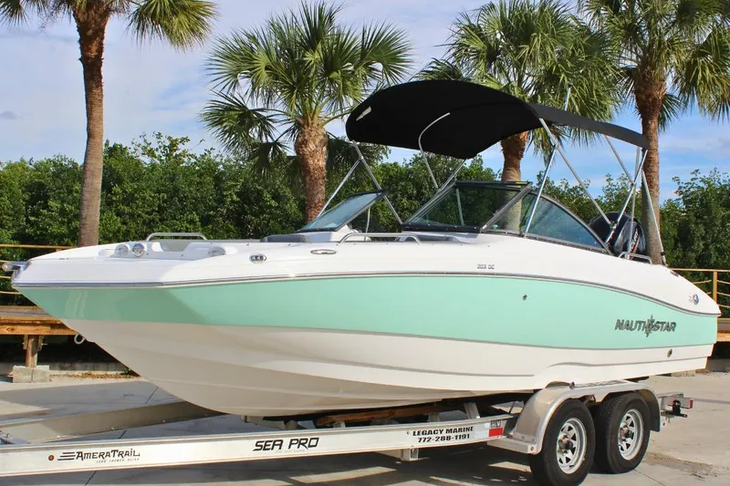 Slide: The Image of 2024 NauticStar 203 DC Deck boat on trailer, surrounded by palm trees. - 13