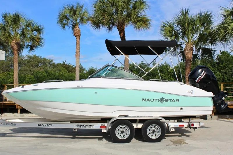 Slide: The Image of 2024 NauticStar 203 DC Deck boat on trailer, palm trees in background. - 14
