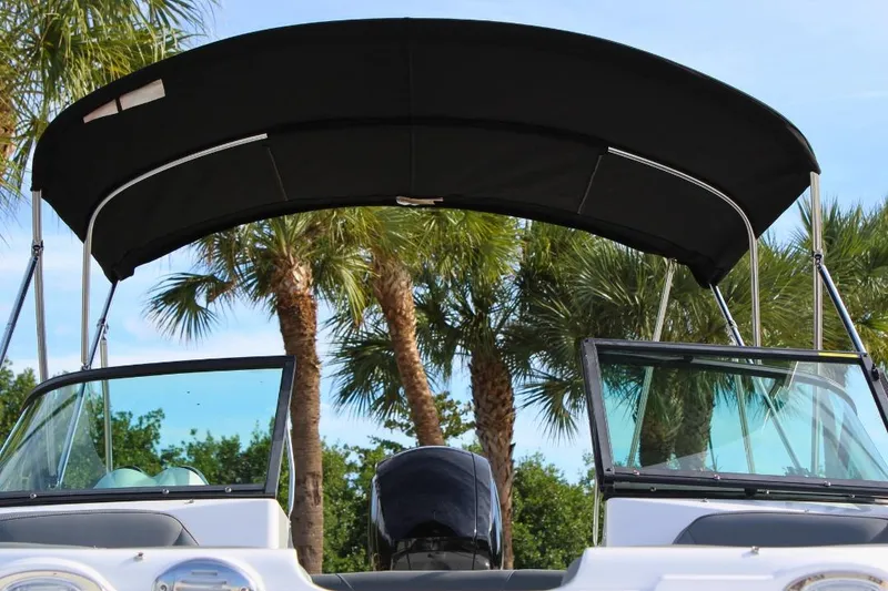 Slide: The Image of 2024 NauticStar 203 DC Deck boat with canopy, surrounded by palm trees. - 16