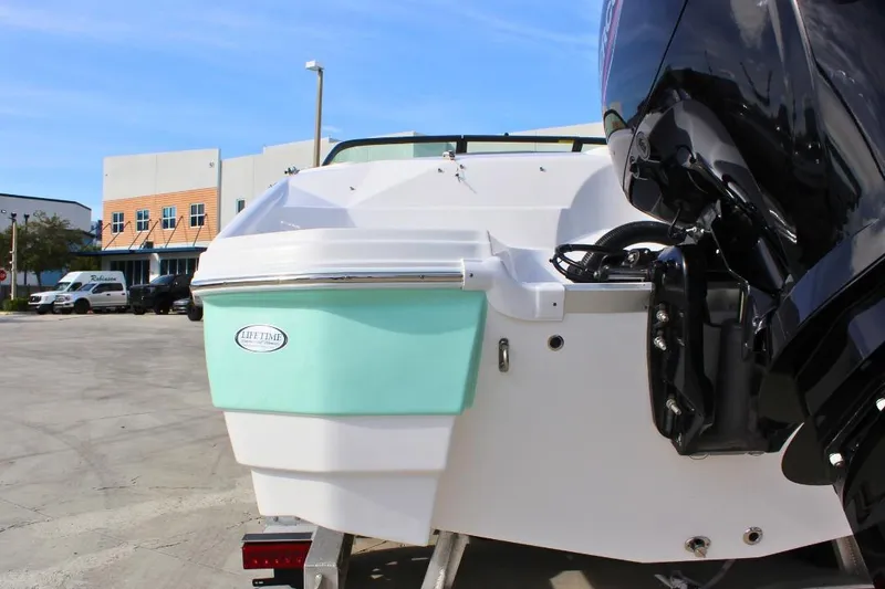 Slide: The Image of 2024 NauticStar 203 DC Deck boat with outboard motor, parked outdoors. - 5