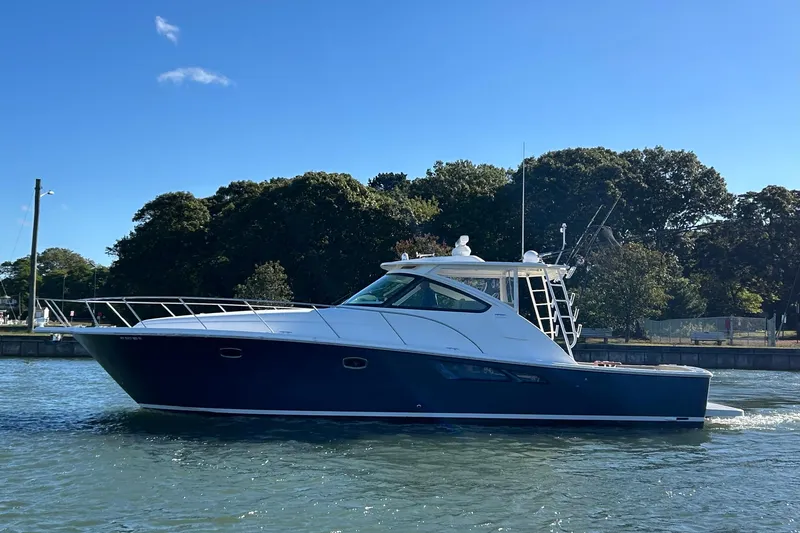 Slide: The Image of 2022 Tiara Yachts 43 Open cruising on a sunny day near a wooded shoreline. - 51