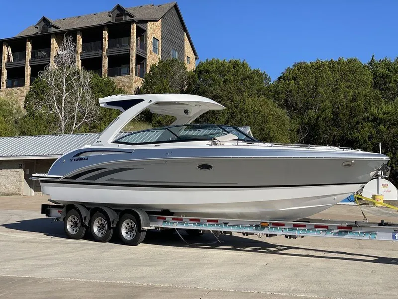 Slide: The Image of 2025 Formula 310 Bowrider on trailer, parked outdoors near trees and buildings. - 21