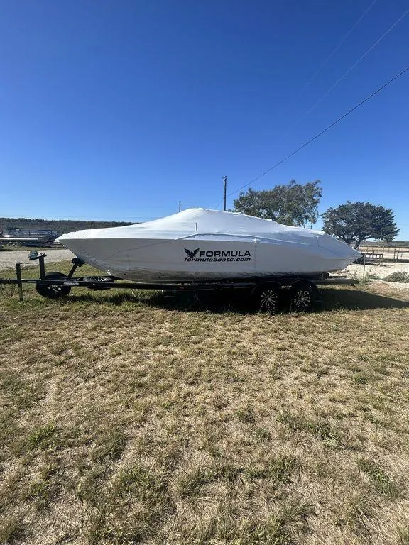 Slide: The Image of 2025 Formula 240 Bowrider boat covered on trailer, parked on grassy field. - 2