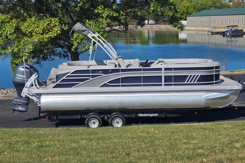 The Image of 2022 Bennington L 22 Quad Bench pontoon boat on trailer by a lake. - 0