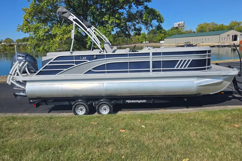 Slide: The Image of 2022 Bennington L 22 Quad Bench pontoon boat on trailer by a lake. - 10