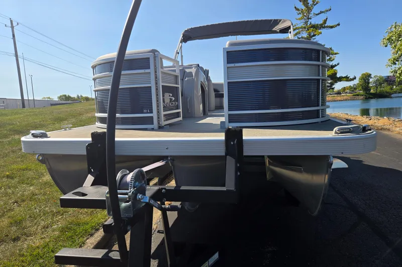 Slide: The Image of 2022 Bennington L 22 Quad Bench pontoon boat on trailer by a lake. - 6