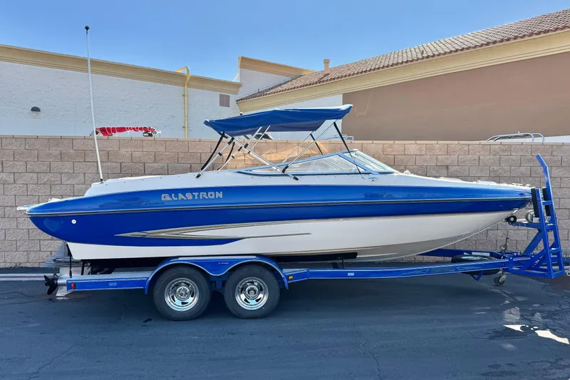 The Image of 2004 Glastron GX 235 boat on trailer, blue and white design, parked outdoors. - 0