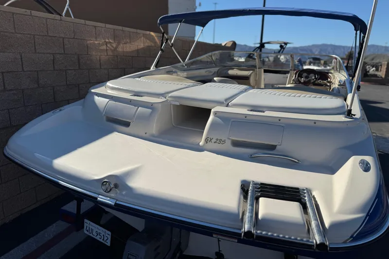 Slide: The Image of 2004 Glastron GX 235 boat with white seating and blue canopy, parked near a brick wall. - 6