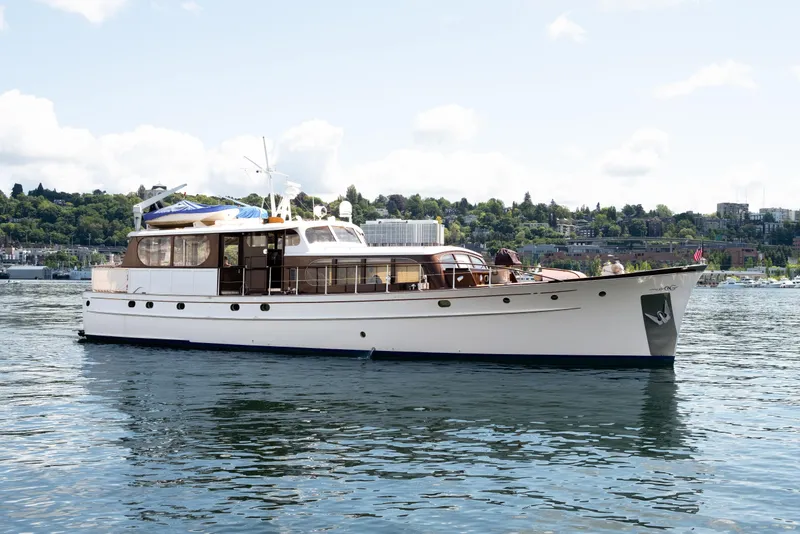 Slide: The Image of A classic 1954 Grebe Sedan yacht on a serene lake with a cityscape backdrop. - 0