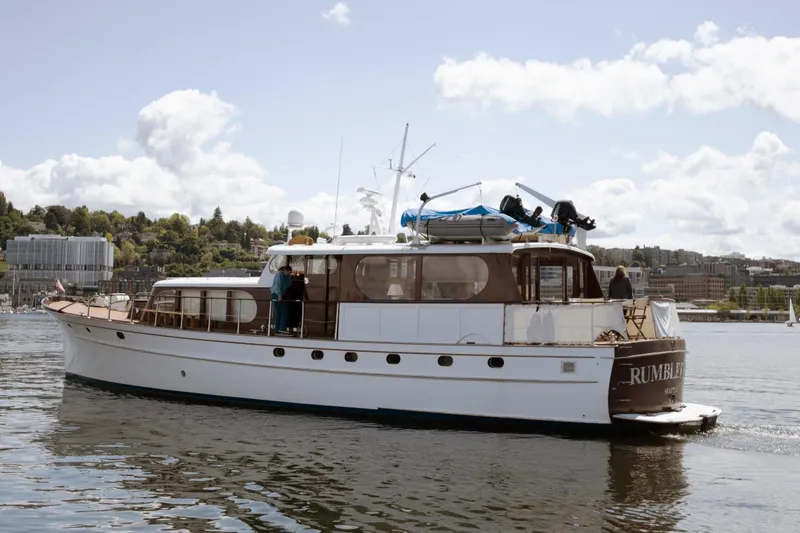 Slide: The Image of A classic yacht named "Rumble" cruising on a sunny day with scenic city backdrop. - 1