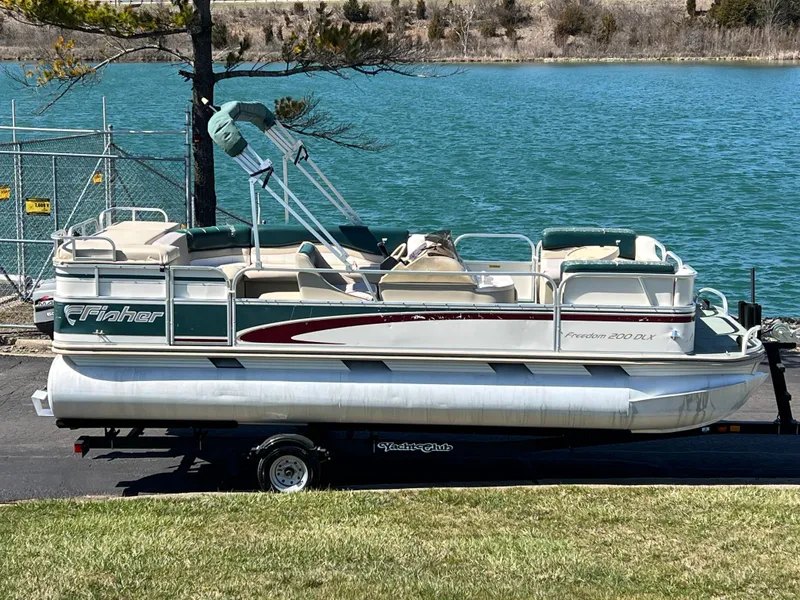 The Image of 1998 Fisher Freedom 200 DLX pontoon boat on trailer by a lake. - 1