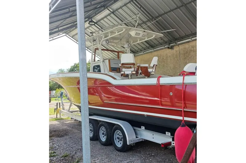 Slide: The Image of 2006 Buddy Davis 34 Center Console boat on trailer, red hull, parked near waterfront. - 2