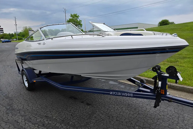 Slide: The Image of 1998 Four Winns 180 Horizon boat on trailer, parked on paved surface, with grassy background. - 5