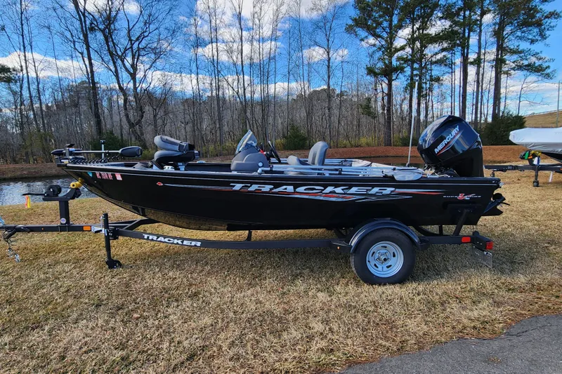 The Image of 2025 Tracker Pro Guide V-16 SC boat on trailer, parked on grass by a pond. - 0