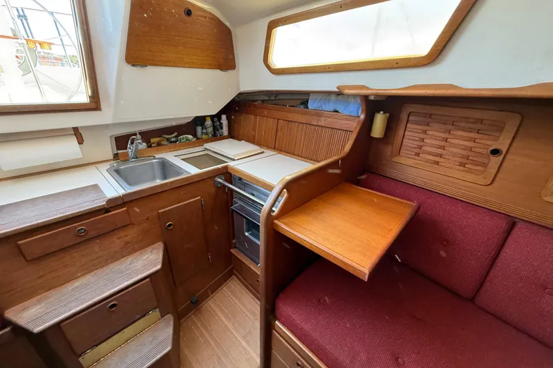 Slide: The Image of 1986 Sabre 30 MKIII yacht interior with wooden cabinetry, sink, stove, and red cushioned seating. - 43