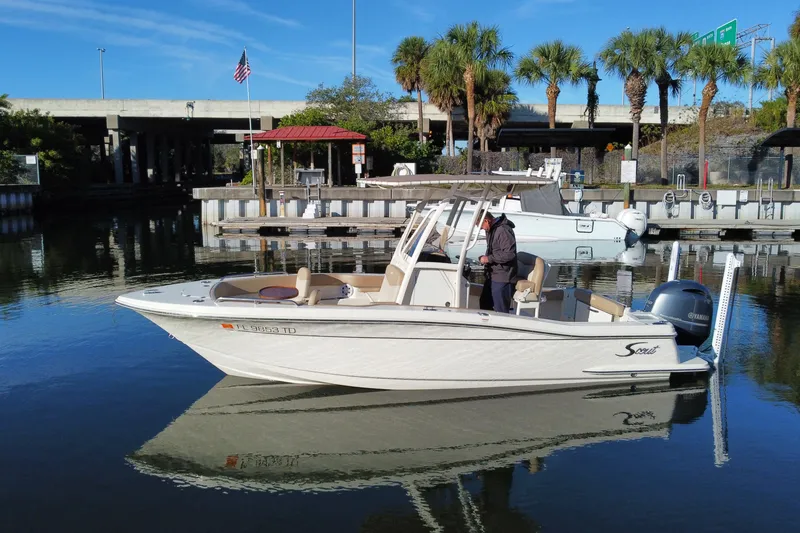 Slide: The Image of 2022 Scout 215 XSF boat docked in a marina with palm trees and clear skies. - 2