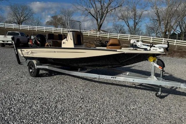 Slide: The Image of 2026 Xpress H20B Bay boat on trailer, parked on gravel with trees and fence in background. - 8