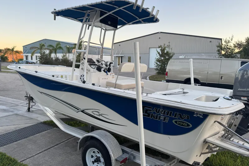 Slide: The Image of 2016 Carolina Skiff 198 DLV boat on trailer, parked outdoors near buildings. - 12