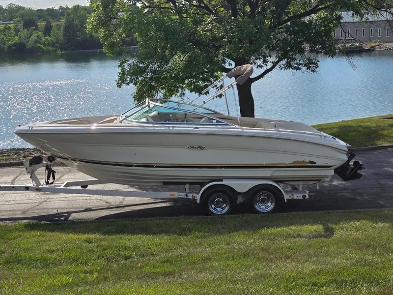 The Image of 1999 Sea Ray 210 BR boat on trailer by a lake, surrounded by greenery. - 0