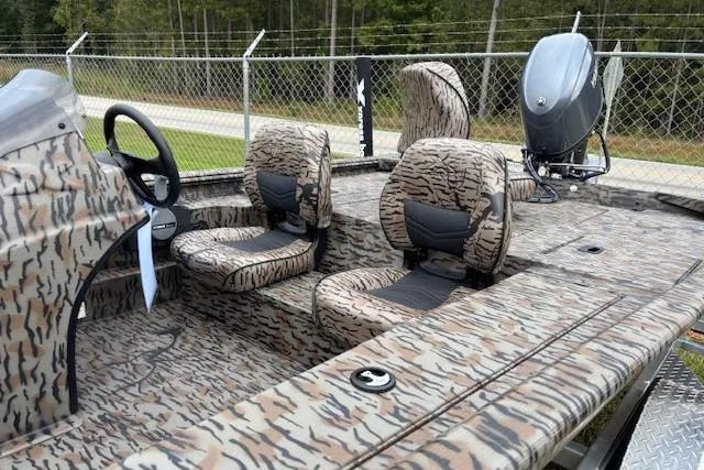 Slide: The Image of 2026 Xpress XP170 boat with camouflage seats and steering, parked near a chain-link fence. - 5