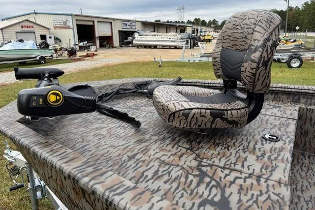 Slide: The Image of 2026 Xpress XP170 boat with camo seating and trolling motor, parked near a workshop. - 6