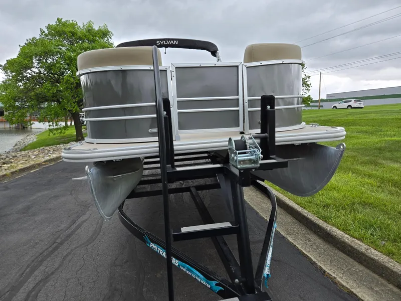Slide: The Image of 2022 Sylvan Mirage Fish 822 Party Fish pontoon boat on trailer, parked near grassy area. - 6