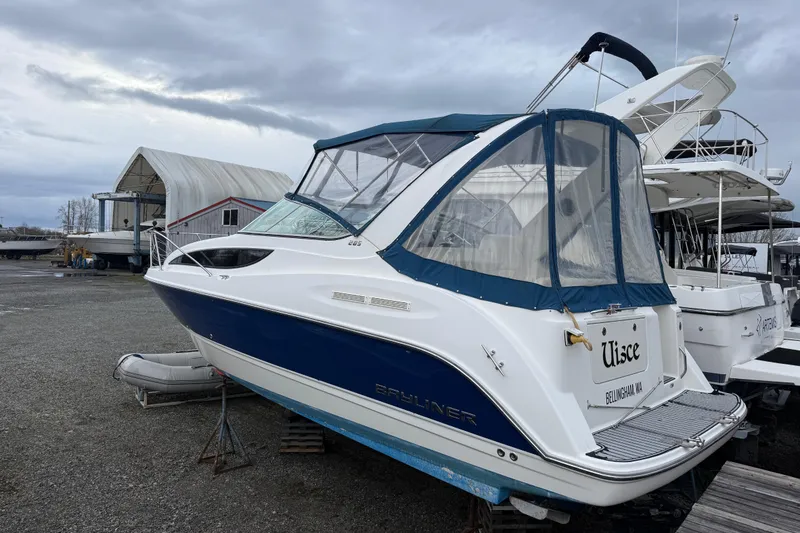 The Image of 2009 Bayliner 285 Cruiser boat on dry dock, blue and white exterior, overcast sky. - 0