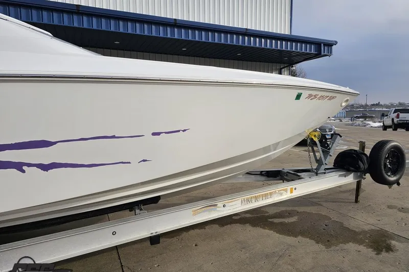 Slide: The Image of 2003 Baja 25 Outlaw boat on trailer with purple graphics, parked outside a building. - 13