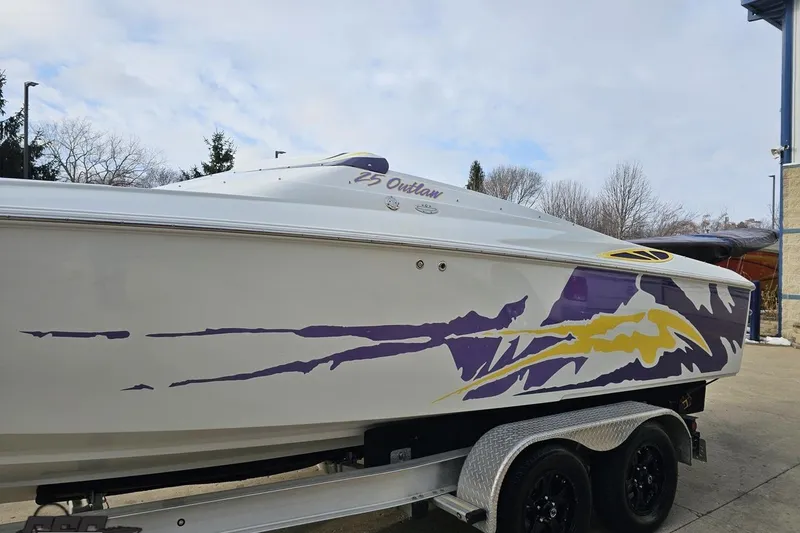 Slide: The Image of 2003 Baja 25 Outlaw boat with vibrant purple and yellow graphics on a trailer. - 18