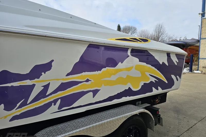 Slide: The Image of 2003 Baja 25 Outlaw boat with vibrant purple and yellow graphics on trailer. - 19