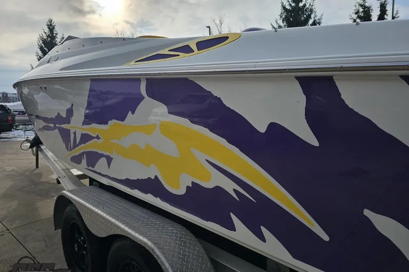 Slide: The Image of 2003 Baja 25 Outlaw boat with vibrant purple and yellow graphics on trailer. - 23