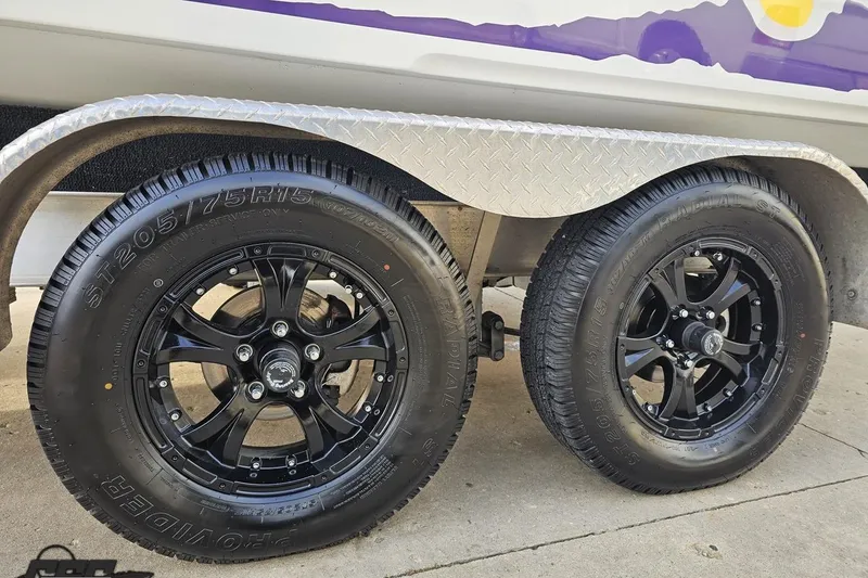 Slide: The Image of Trailer wheels of a 2003 Baja 25 Outlaw boat with black rims and radial tires. - 24