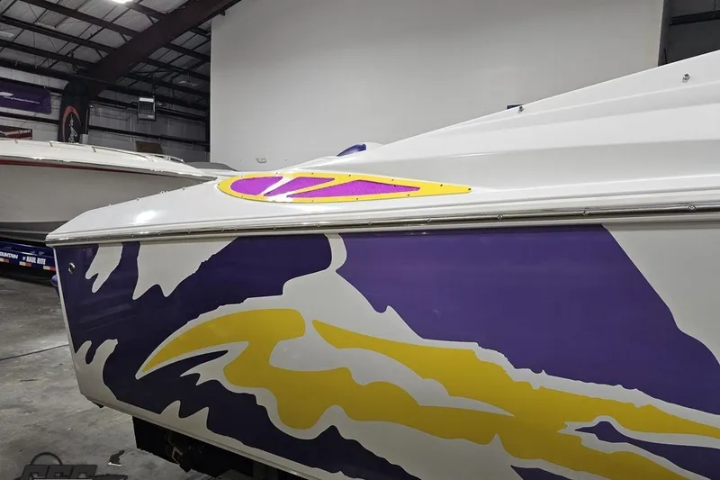 Slide: The Image of 2003 Baja 25 Outlaw boat with vibrant purple and yellow graphics in a warehouse. - 41