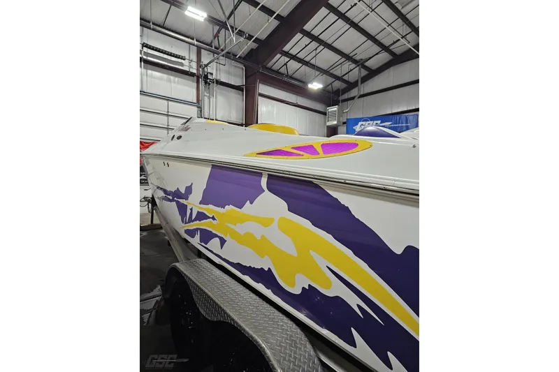 Slide: The Image of 2003 Baja 25 Outlaw boat with vibrant purple and yellow graphics in a warehouse. - 44