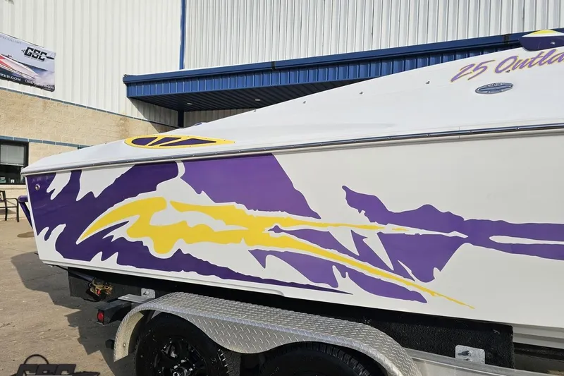 Slide: The Image of 2003 Baja 25 Outlaw boat with vibrant purple and yellow graphics on trailer. - 7