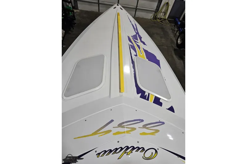 Slide: The Image of 2003 Baja 25 Outlaw boat with vibrant yellow and purple graphics in a garage. - 90