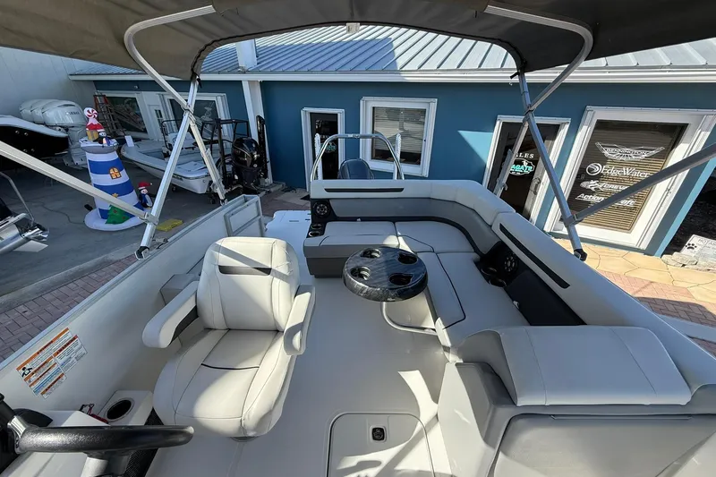 Slide: The Image of 2023 Hurricane FunDeck 2260 RE OB boat interior with seating and table, docked near blue building. - 17