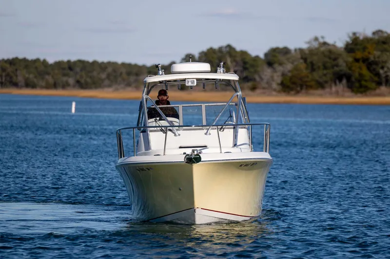 Slide: The Image of 2006 Sailfish 2660 WAC boat cruising on a calm lake with forested shoreline. - 7